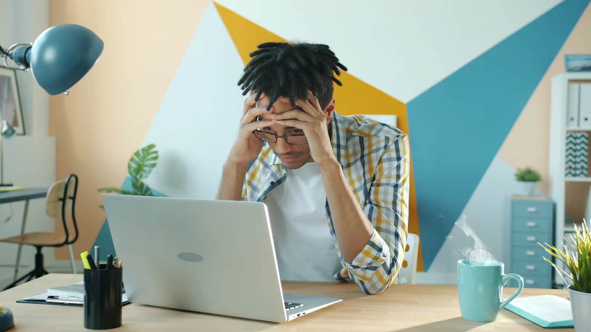 Man holding his head in frustration at a desk with a laptop
